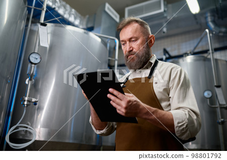 Handsome bearded man brewer inside modern beer factory around steel tanks 98801792