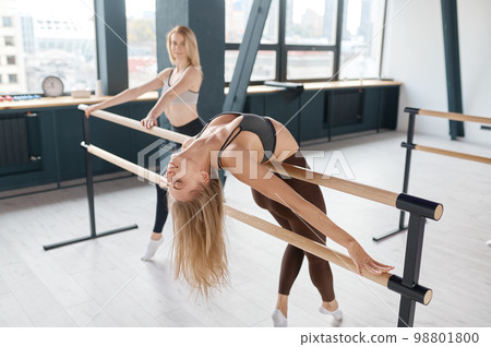 Beautiful graceful woman performing ballet exercises using bar at gym 98801800