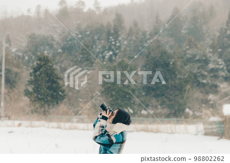Photo of a young woman holding a camera in the snow 98802262