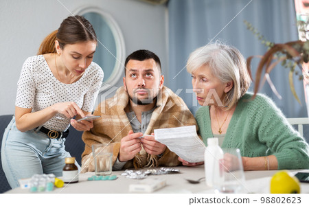 Elderly mother and a young wife give pills and medicines to her husband during illness 98802623