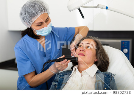Beautician with client during hardware facial procedure in clinic Beautician with client during hardware facial procedure in clinic 98802728