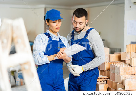 Man and woman builders discussing project documentation Man and woman builders discussing project documentation 98802733