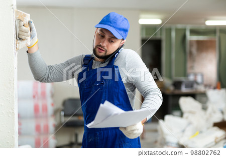 Master with documents plasters the wall of a house, talking on the phone Master with documents plasters the wall of a house, talking on the phone 98802762
