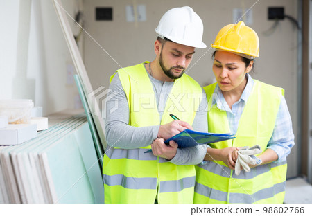 Man and woman builders discussing project documentation Man and woman builders discussing project documentation 98802766