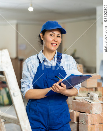 Female builder fills out documentation during repair work Female builder fills out documentation during repair work 98802803