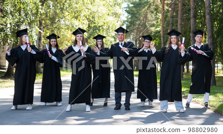 Group of graduates in robes dancing outdoors. Elderly student. Group of graduates in robes dancing outdoors. Elderly student. 98802980