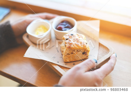 scones and jam on wooden plate, woman served scones and cream for dessert and tea - fresh homemade butter scones 98803468