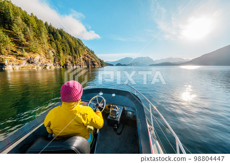 Woman Driving Motor Boat in Amazing Nature Landscape at Sunset in Coastal British Columbia Near Bute, Toba Inlet and Campbell River. Whale Watching Tourist Travel Destination, Canada 98804447