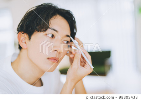 man drawing eyebrows with eyebrow pencil 98805438
