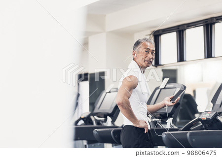 Senior man using running machine while enjoying music Senior man using running machine while enjoying music 98806475