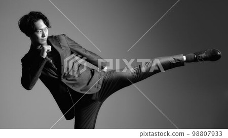 A business person in a suit taking a high kick pose Monochrome image 98807933