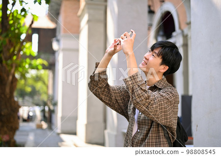 Handsome young Asian man tourist taking a picture with his smartphone. vacation, traveling 98808545