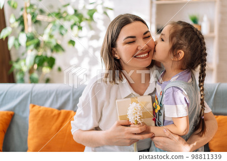 Daughter kissed her mother and gave gift with flowers while sitting on the sofa, mother's day 98811339