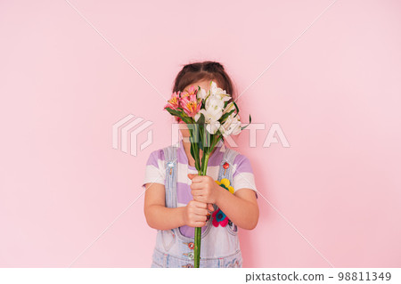 Little girl in overalls holding flowers against pink background, mother's day Little girl in overalls holding flowers against pink background, mother's day 98811349