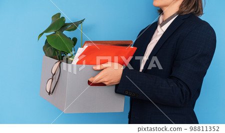 Girl in white shirt and jacket holding box with office supplies and flower in her hands Girl in white shirt and jacket holding box with office supplies and flower in her hands 98811352
