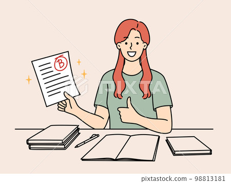 Happy girl student rejoices at average mark for test sits at table with books and pen Happy girl student rejoices at average mark for test sits at table with books and pen 98813181