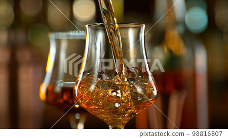 Close-up of pouring whiskey or rum on the bar, dark toned background Close-up of pouring whiskey or rum on the bar, dark toned background 98816807