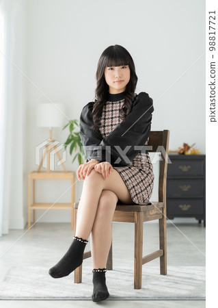 Portrait of a Gen Z girl sitting on a chair in her living room and looking at the camera 98817721