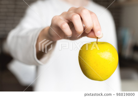 close-up, a woman's hand holds an apple by the tail hanging, the background is blurred. unrecognizable person close-up, a woman's hand holds an apple by the tail hanging, the background is blurred. unrecognizable person 98819800