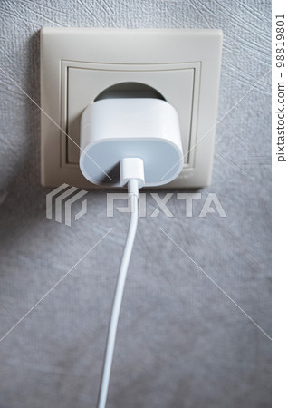 Phone charger in an electrical socket on the wall, close-up, vertical photo Phone charger in an electrical socket on the wall, close-up, vertical photo 98819801