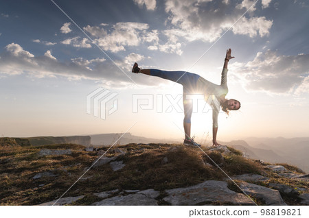 Young woman doing beautiful yoga, sunset or sunrise in mountains over blue sky and clouds against sunlight. Healthy lifestyle successful fitness exercise concept 98819821