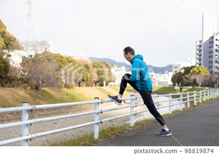 A middle-aged man stretching his legs and doing warm-up exercises before running as a hobby A middle-aged man stretching his legs and doing warm-up exercises before running as a hobby 98819874