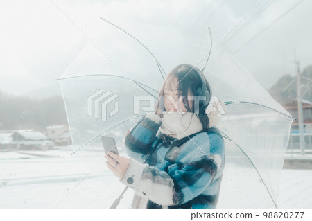 Photo of a young woman listening to music on her smartphone in the snow Photo of a young woman listening to music on her smartphone in the snow 98820277