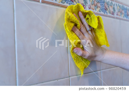 Woman's hands cleaning the tiles with a yellow rag. Space for text. Woman's hands cleaning the tiles with a yellow rag. Space for text. 98820459