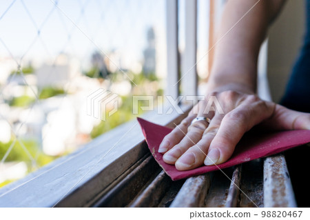 Normal view of a woman's hands sanding a window frame before painting. Empowered woman concept. Normal view of a woman's hands sanding a window frame before painting. Empowered woman concept. 98820467