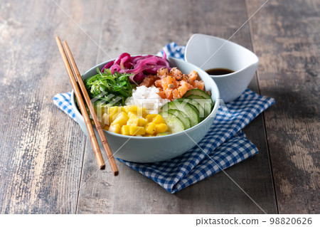 Poke bowl with rice, salmon,cucumber,mango,onion,wakame salad, poppy seeds ands sunflowers seeds on wooden background Poke bowl with rice, salmon,cucumber,mango,onion,wakame salad, poppy seeds ands sunflowers seeds on wooden background 98820626
