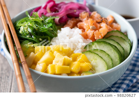 Poke bowl with rice, salmon,cucumber,mango,onion,wakame salad, poppy seeds ands sunflowers seeds on wooden background Poke bowl with rice, salmon,cucumber,mango,onion,wakame salad, poppy seeds ands sunflowers seeds on wooden background 98820627