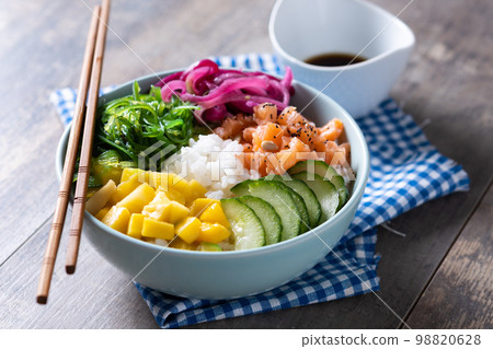 Poke bowl with rice, salmon,cucumber,mango,onion,wakame salad, poppy seeds ands sunflowers seeds on wooden background Poke bowl with rice, salmon,cucumber,mango,onion,wakame salad, poppy seeds ands sunflowers seeds on wooden background 98820628