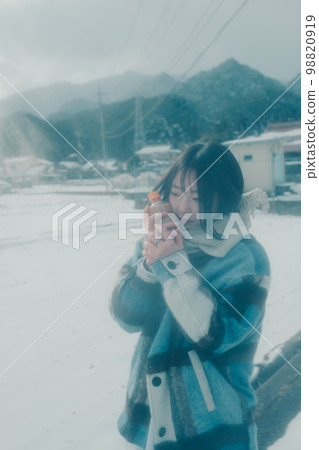 Photo of a young woman having a warm drink in the snow Photo of a young woman having a warm drink in the snow 98820919