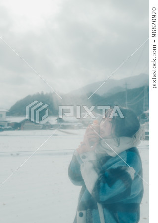 Photo of a young woman having a warm drink in the snow Photo of a young woman having a warm drink in the snow 98820920