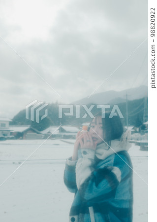 Photo of a young woman having a warm drink in the snow Photo of a young woman having a warm drink in the snow 98820922