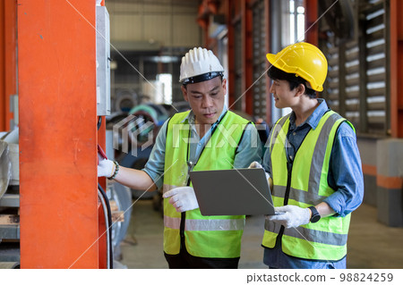 Two man industrial engineers wear hard hats and uniform using laptop learning project. 98824259