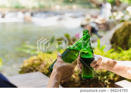 Senior man toasting with bottle beer together with his son on vacation. Senior man toasting with bottle beer together with his son on vacation. 98824795
