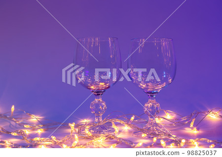 Two wine glasses and a garland in neon lighting, Valentines day background. Two wine glasses and a garland in neon lighting, Valentines day background. 98825037