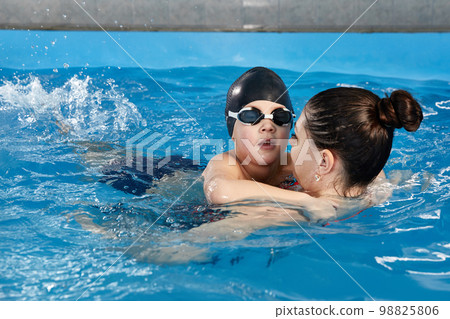 Little boy learning to swim in pool with teacher Little boy learning to swim in pool with teacher 98825806