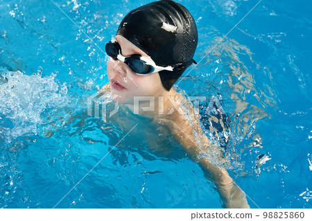 Preschool boy learning how to swim in a pool wearing swimming cap and goggles 98825860