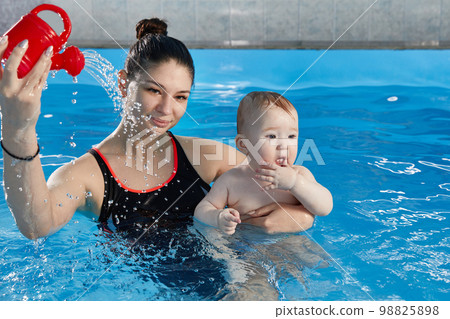 Little baby learning to swim in pool with teacher 98825898