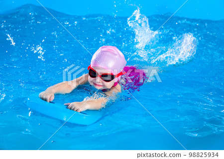 Preschool cute girl learning to swim in indoor pool with flutter board Preschool cute girl learning to swim in indoor pool with flutter board 98825934