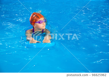 Little girl learning how to swim in a pool using flutterboard with copy space 98825962