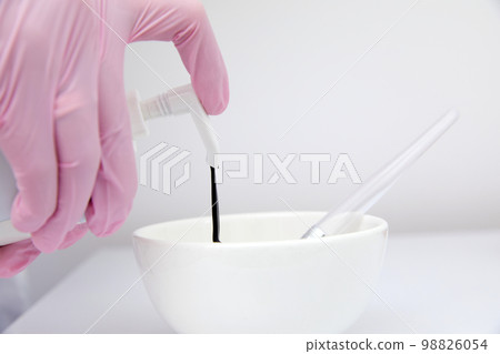 Close up of cosmetologist filling up a container with black face mask for carbon peeling Close up of cosmetologist filling up a container with black face mask for carbon peeling 98826054