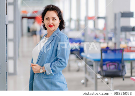 a brunette woman in a blue jacket in a workspace with open offices.  98826098