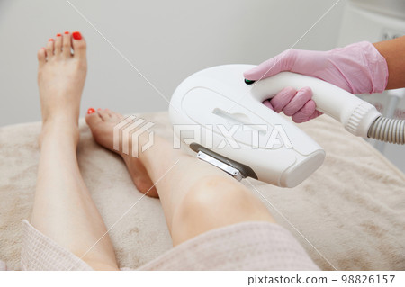 Partial view of woman receiving laser hair removal epilation on leg in a salon 98826157