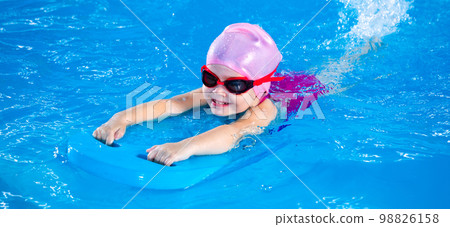 Panorama of Smiling little girl learning to swim in pool with flutterboard during swimming class Panorama of Smiling little girl learning to swim in pool with flutterboard during swimming class 98826158
