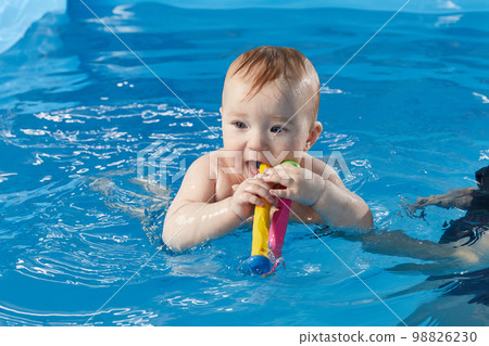 Little baby learning to swim in pool with trainer Little baby learning to swim in pool with trainer 98826230