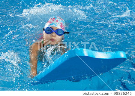 Little girl learning to swim in indoor pool with pool board 98826245