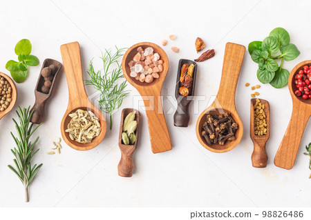 Various spices and green herbs in wooden spoons on white table Various spices and green herbs in wooden spoons on white table 98826486